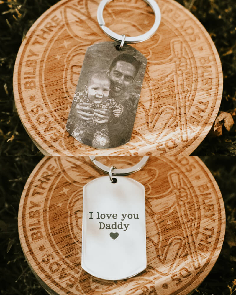 Stainless Steel keychain with engraved text and photo of a man and child, on a natural background.