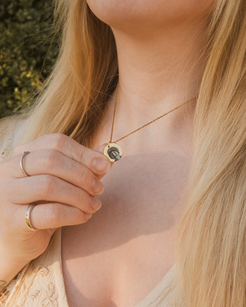 Close-up of a person wearing a gold necklace with a pendant, held by a hand.