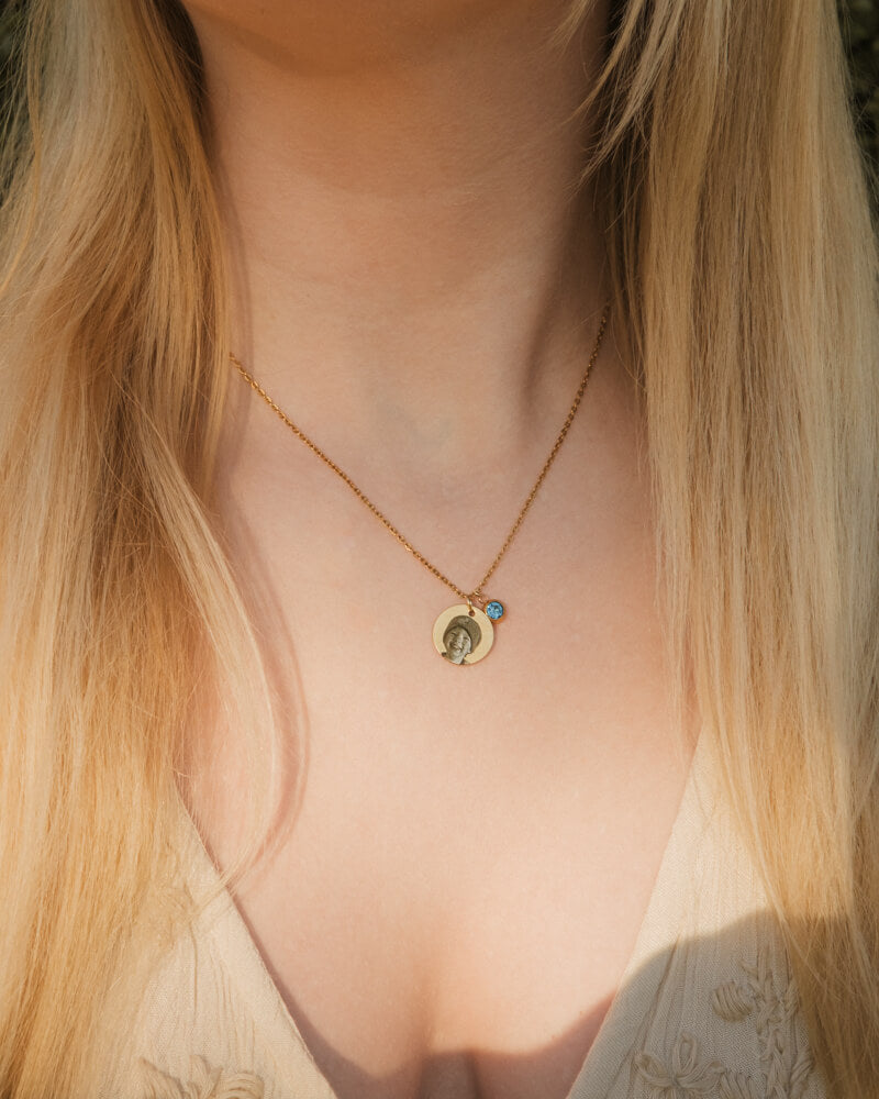 Gold necklace with a pendant worn by a person with long blonde hair.