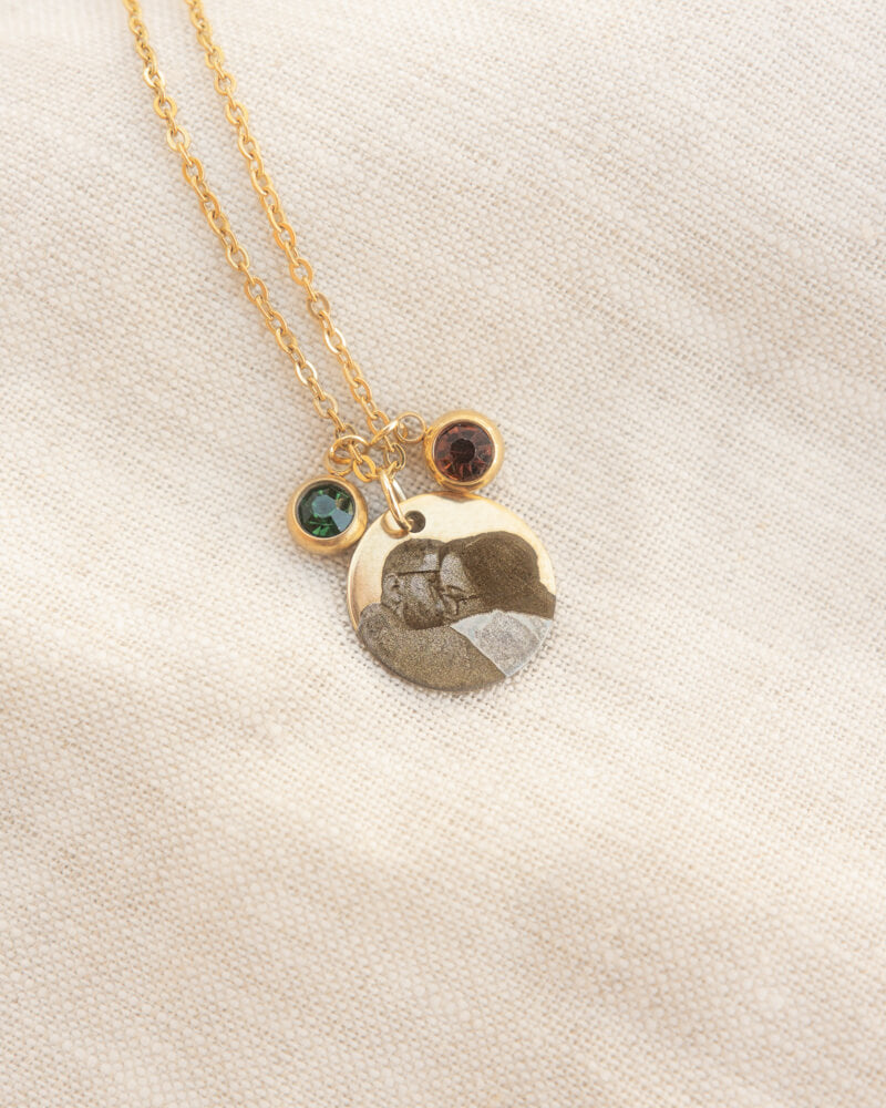 Gold necklace with two charms on a light beige background