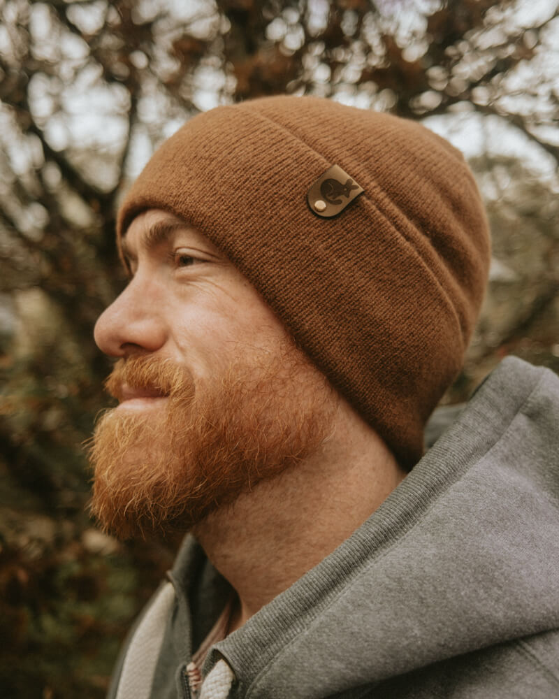 Man wearing a brown beanie and gray coat with a blurred natural background