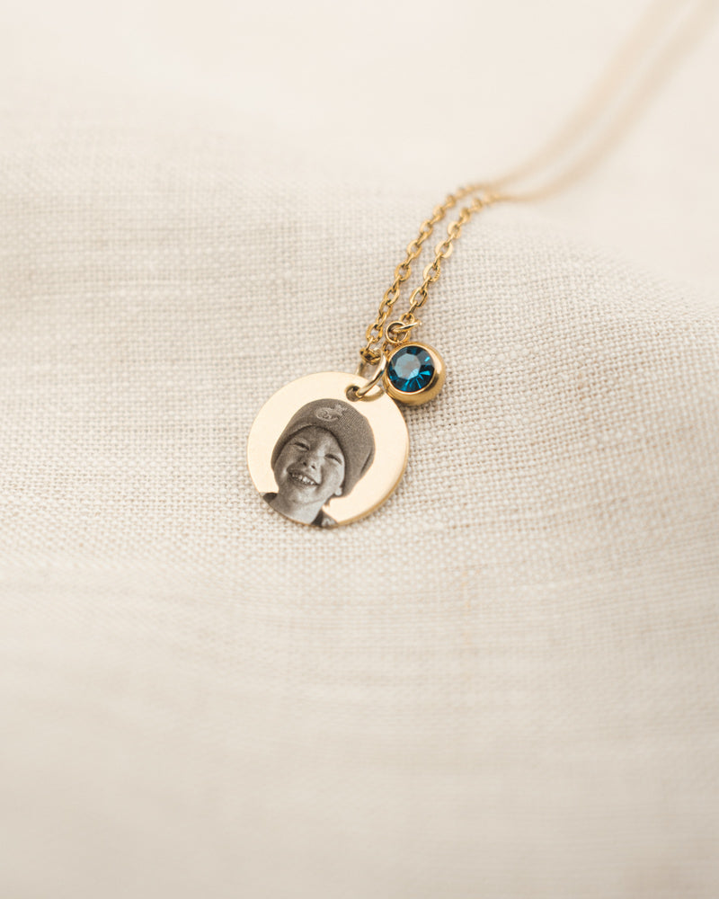 Gold necklace with a pendant featuring a photo of a child on a beige fabric background