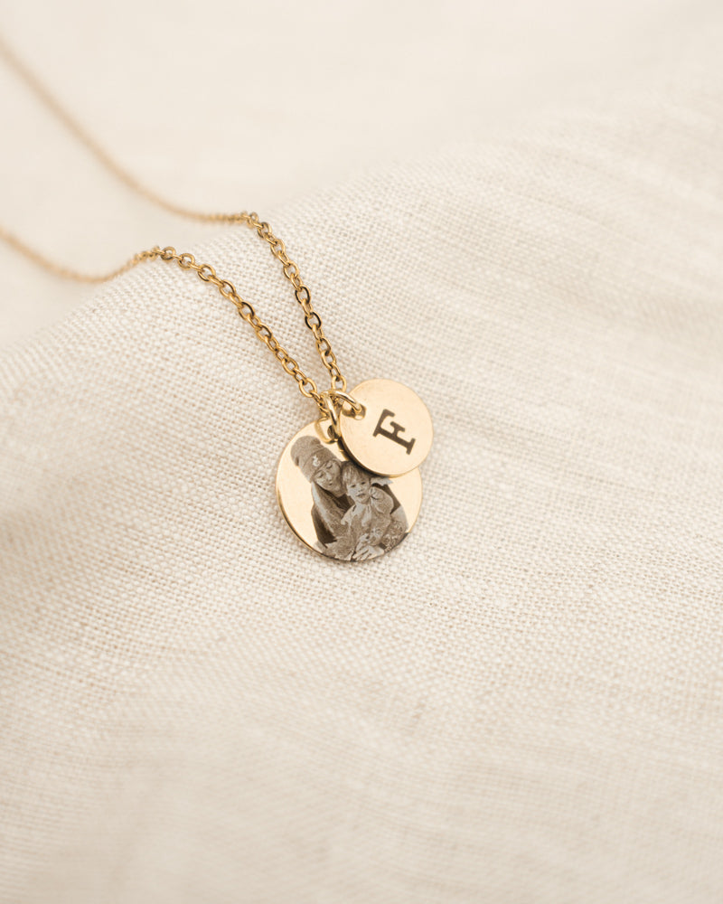 Gold necklace with two round pendants on a beige fabric background